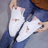 White low-top sneakers with pink accents, tassel charms, and casual fit, shown with jeans.