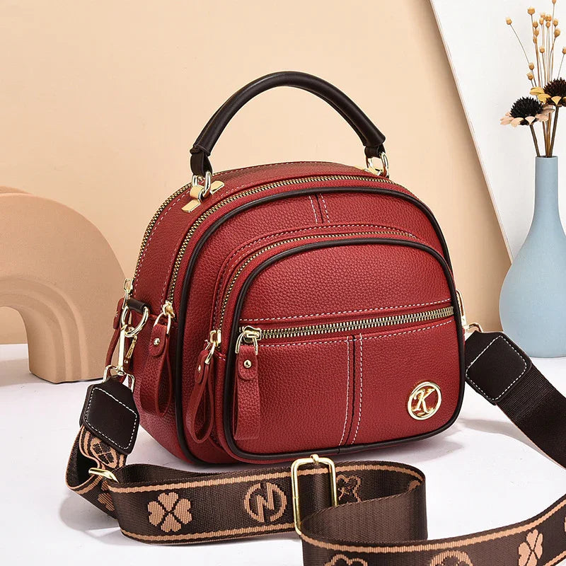 Red faux leather crossbody bag with gold zippers, top handle, and adjustable strap
