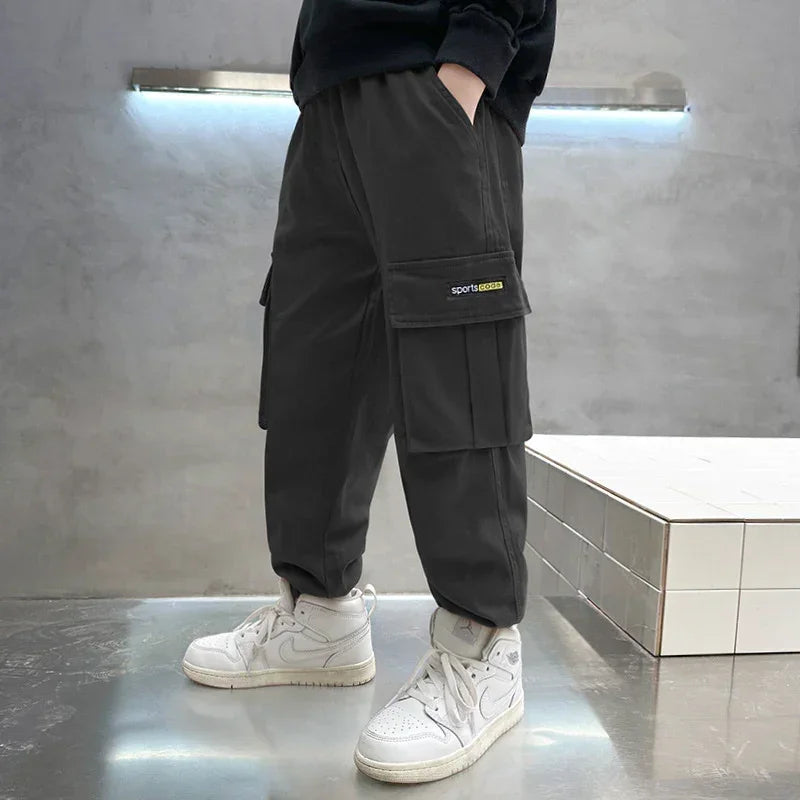 Black cargo pants with large side pockets, relaxed fit, paired with white sneakers.