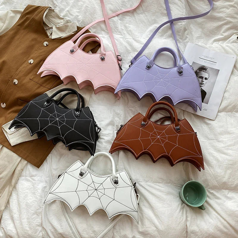 Assorted bat wing handbags in black, white, brown, pink, and lavender vegan leather with spiderweb stitching, unique streetwear accessories, displayed on a bed.