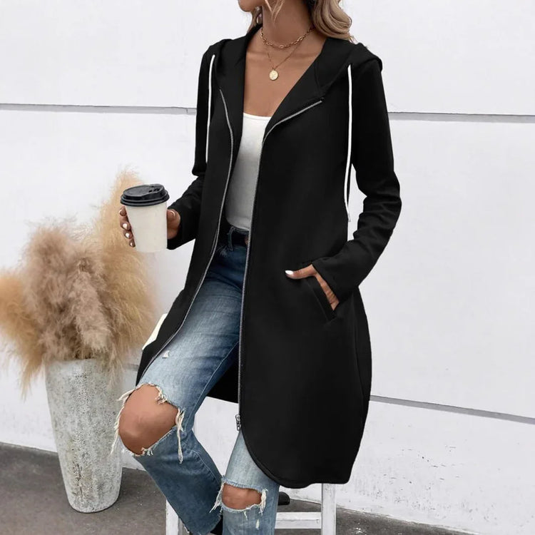 Woman wearing a black long hoodie coat, white tank top, ripped blue jeans, casual streetwear style.