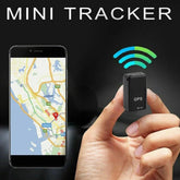 Hand holding black mini GPS tracker device near smartphone showing map location