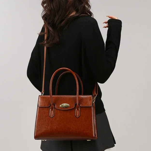 Woman wearing a black long-sleeve top and skirt, carrying a brown leather satchel crossbody bag.