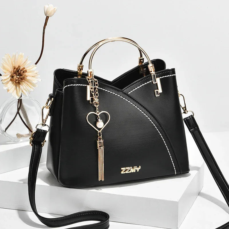 Black faux leather handbag with gold hardware, heart charm, white stitching, structured fit