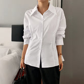 Woman wearing a white button-up cotton shirt with long sleeves and a tailored fit, paired with black pants.