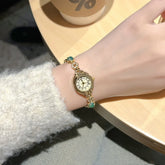 Gold vintage bracelet watch with Roman numerals and green gemstone accents on wrist