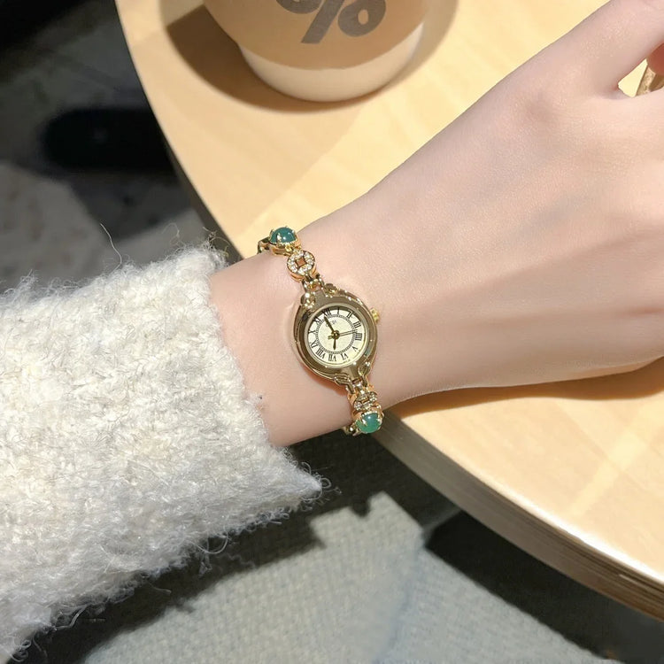 Gold vintage bracelet watch with Roman numerals and green gemstone accents on wrist