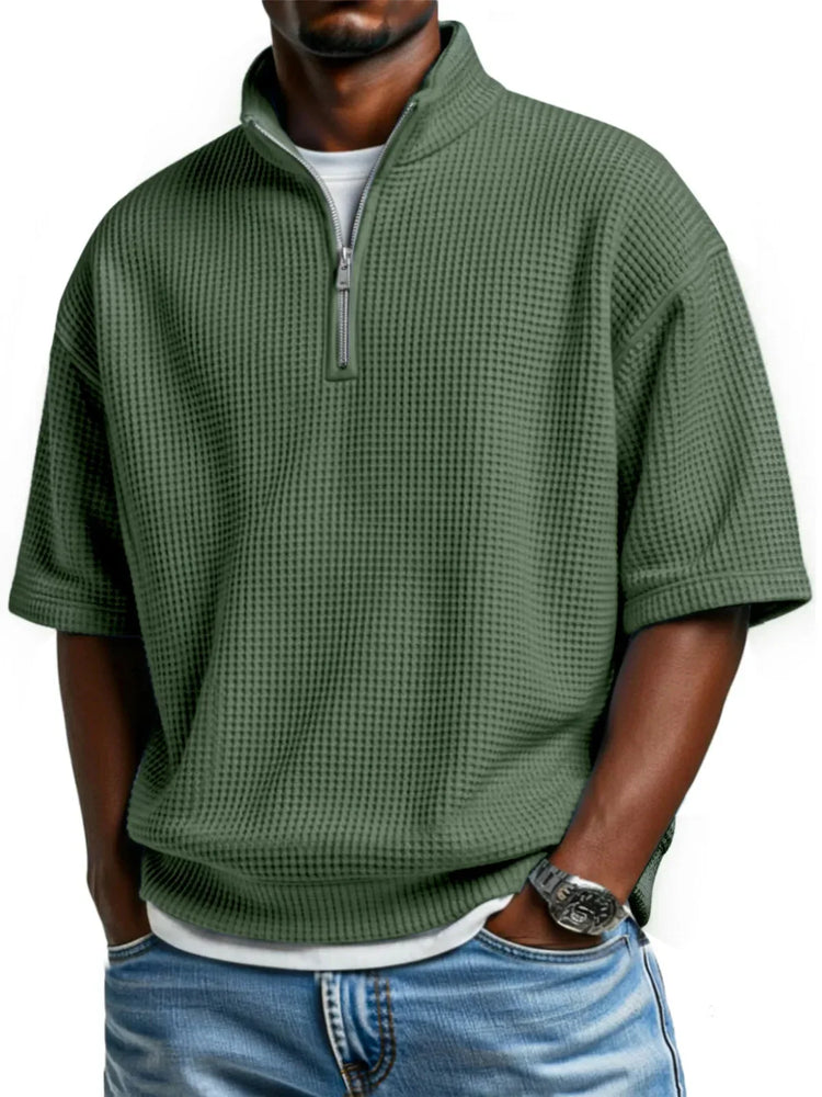 Man wearing loose fit green waffle knit short sleeve pullover with half zip, blue jeans