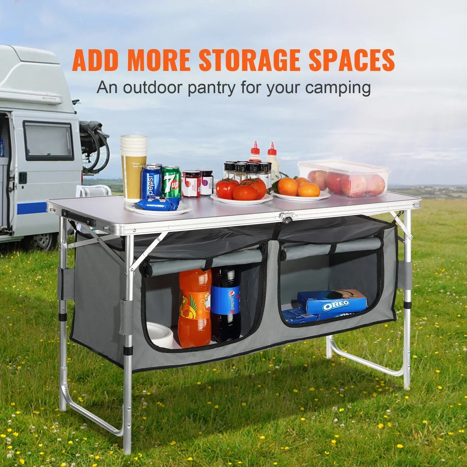 Collapsible outdoor camping pantry table with aluminum frame, gray fabric storage shelves, and assorted groceries, set on grass near a camper van.