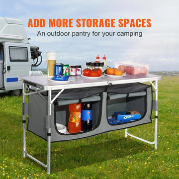Collapsible outdoor camping pantry table with aluminum frame, gray fabric storage shelves, and assorted groceries, set on grass near a camper van.