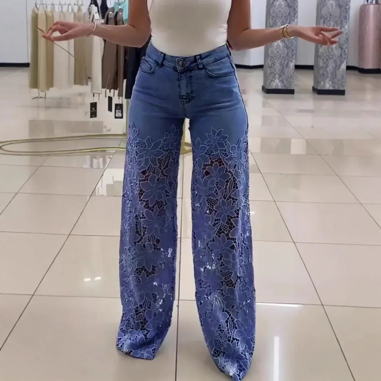 Woman wearing blue wide-leg denim pants with sheer lace floral panels and a fitted white tank top