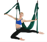 Woman in blue sports bra and black leggings performing aerial yoga on green hammock