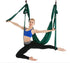 Woman in blue sports bra and black leggings performing aerial yoga on green hammock