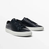 Black leather low-top sneakers with white rubber soles and lace-up closure, minimalist style