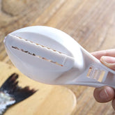 White plastic fish scaler tool with serrated blade and ergonomic handle on wooden surface