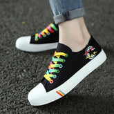 Black canvas sneakers with rainbow laces, white soles, and streetwear graphic detail