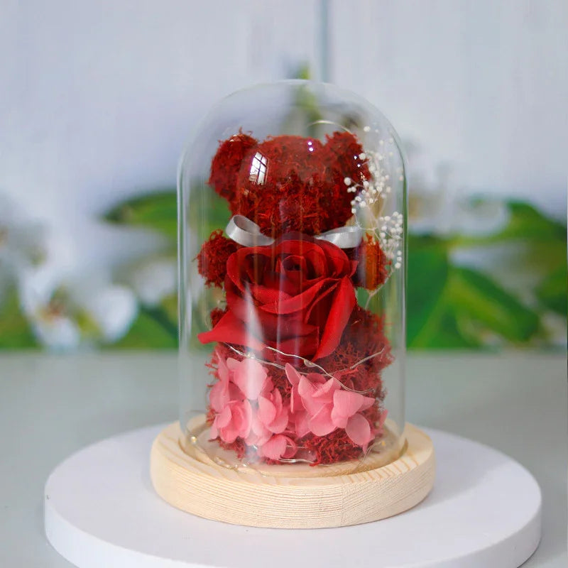Red preserved rose teddy bear with pink petals in a glass dome on wooden base, decorative gift