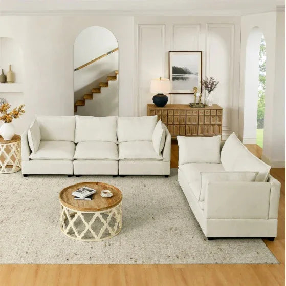 Modern living room with two cream-colored fabric sofas, wooden round coffee table, and neutral decor accents.