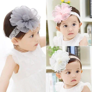 Baby wearing sleeveless white dress with lace headbands featuring large fabric flower accents in pink, grey, and white.