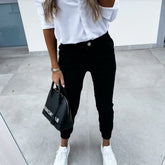 Woman wearing white shirt, black jogger pants, white sneakers, holding black handbag