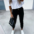 Woman wearing white shirt, black jogger pants, white sneakers, holding black handbag