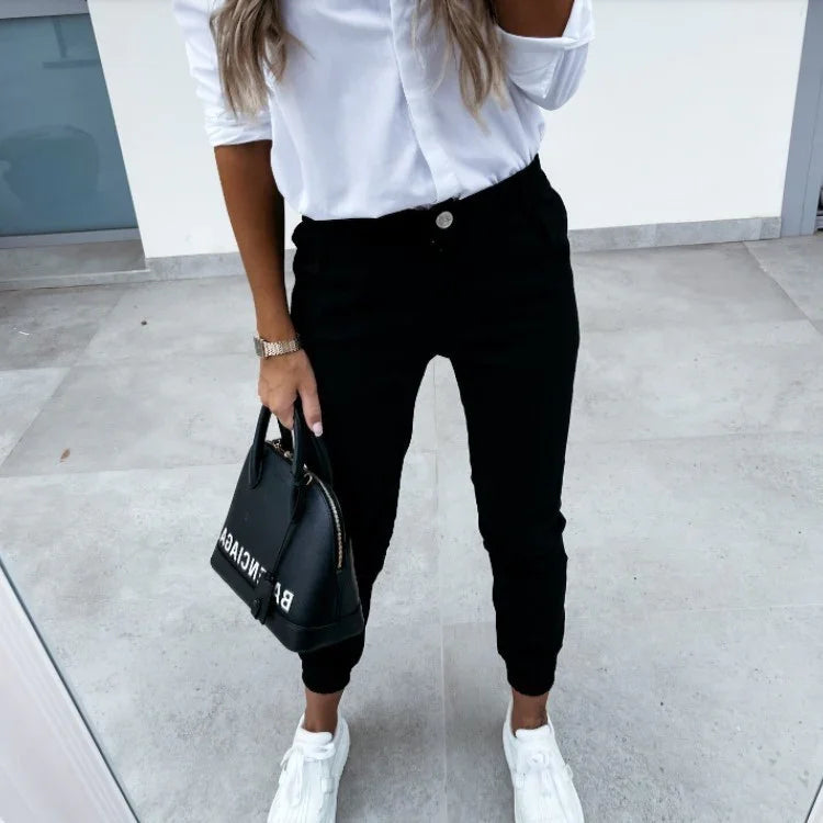 Woman wearing white shirt, black jogger pants, white sneakers, holding black handbag
