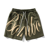 Olive green streetwear shorts with beige graphic text, drawstring waist, relaxed fit