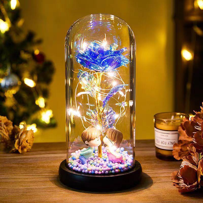 Decorative glass dome with blue artificial rose, fairy lights, and couple figurines on a wooden table