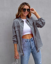 Woman wearing a distressed grey denim jacket, white crop top, and high-waisted blue jeans