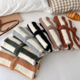 Striped fuzzy sweaters in beige, black, green, brown, and gray, folded on a bed.