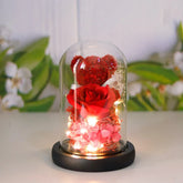 Red preserved rose and floral arrangement with a teddy bear in a glass dome with fairy lights