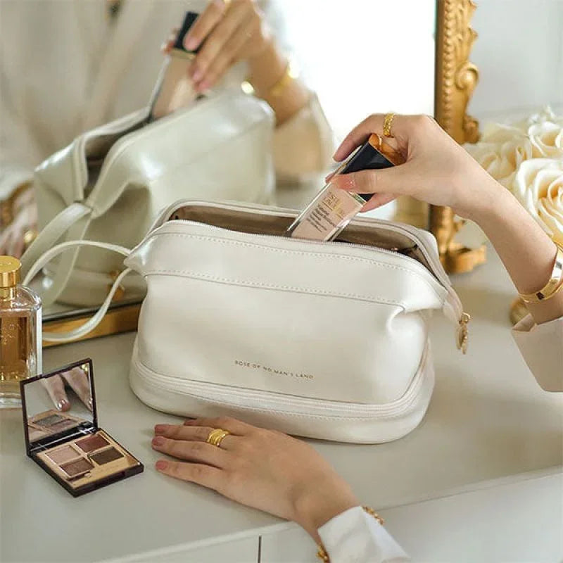 Cream faux leather cosmetic bag with gold hardware, shown on a vanity with makeup products