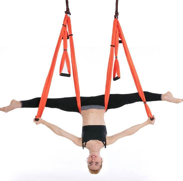 Woman in black athletic wear performing splits on orange aerial yoga hammock