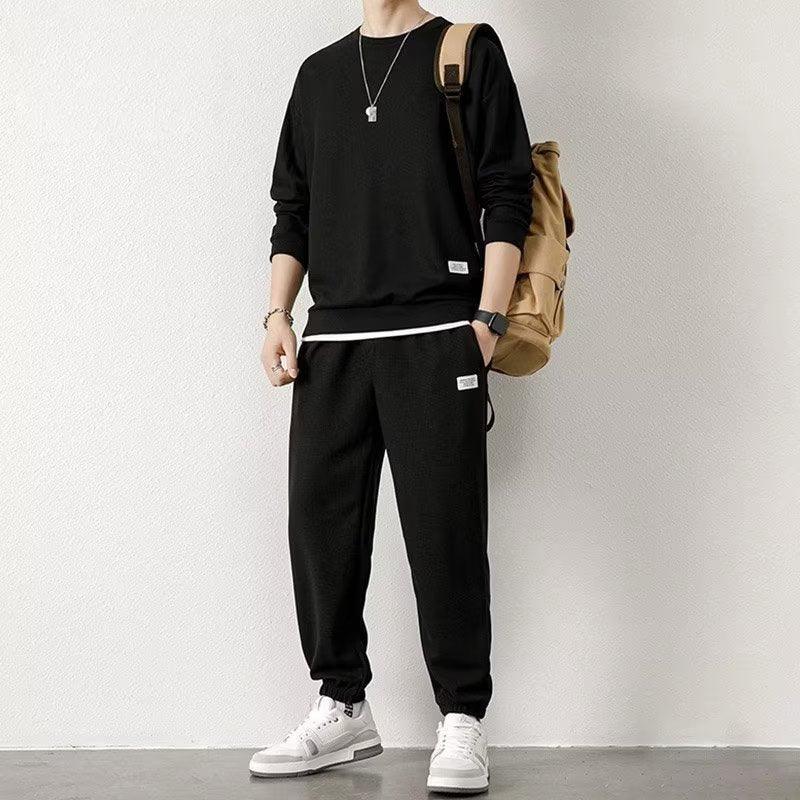 Man wearing black streetwear tracksuit set, relaxed fit, with white sneakers and tan backpack