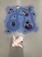 Blue space-themed kids puzzle mat with cartoon astronauts, aliens, rockets, and a toy airplane.