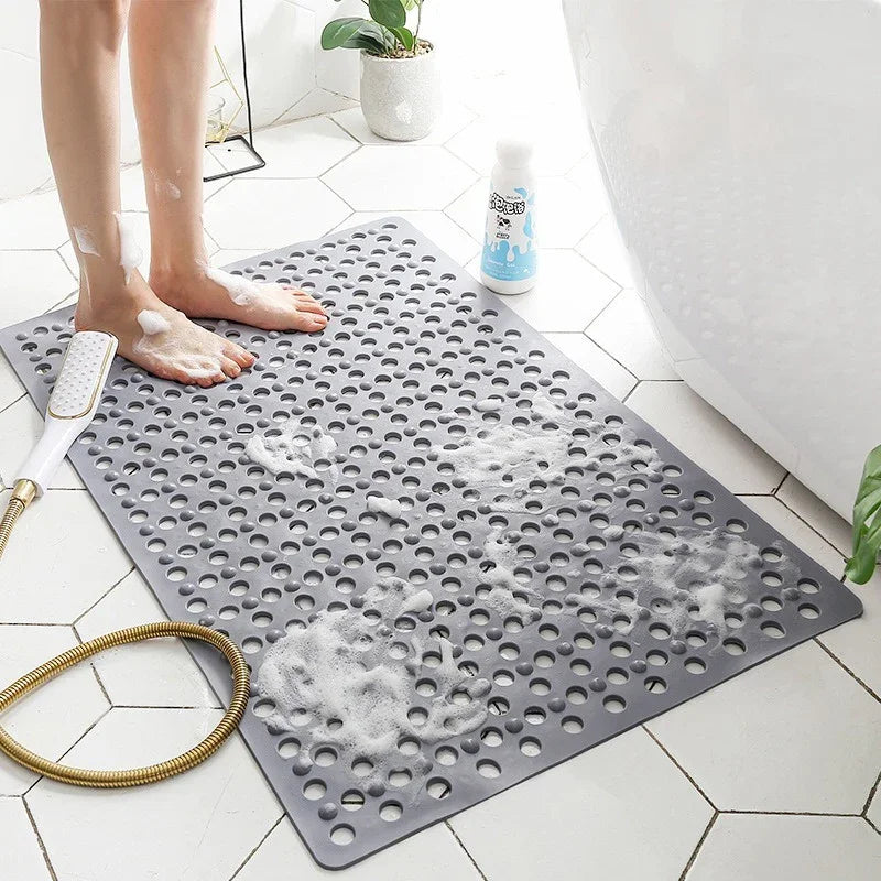 Gray non-slip rubber bath mat with drain holes in modern bathroom, person washing feet