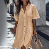 Woman wearing loose beige linen shirt dress with short sleeves and front buttons, holding straw bag