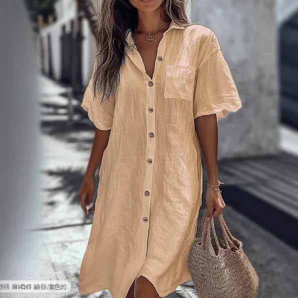 Woman wearing loose beige linen shirt dress with short sleeves and front buttons, holding straw bag