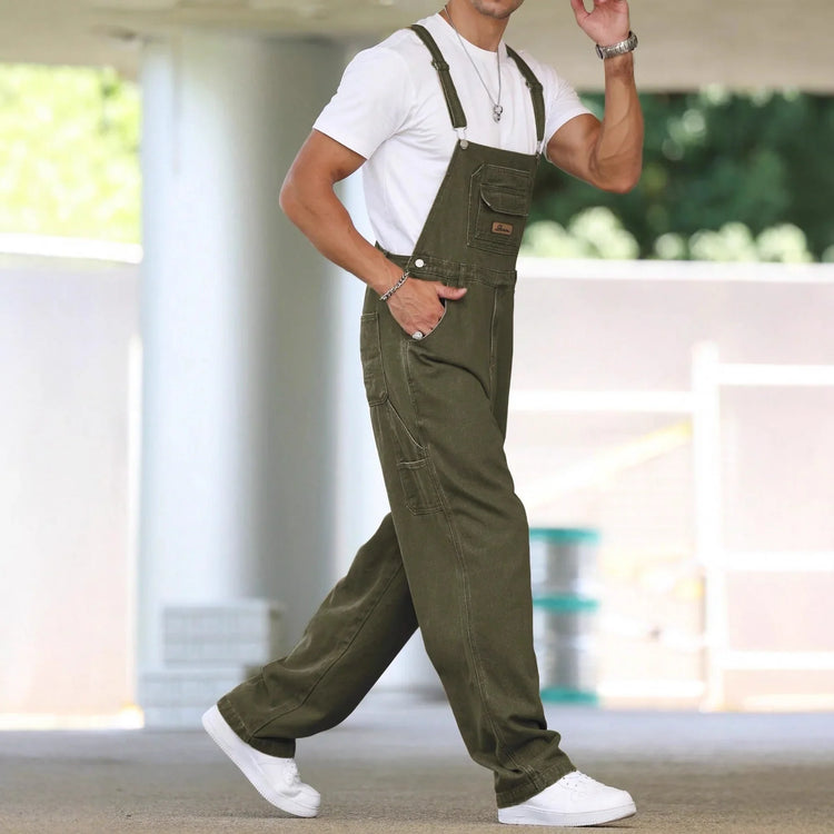 Man wearing loose fit olive green denim overalls with a white t-shirt and white sneakers