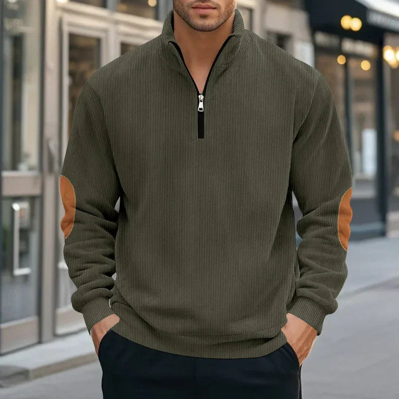 Man wearing olive green ribbed pullover with half-zip, brown suede elbow patches, relaxed fit.