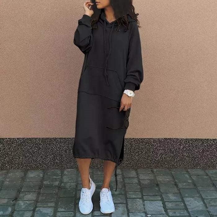 Woman wearing a black oversized hoodie dress with long sleeves and white sneakers, casual fit