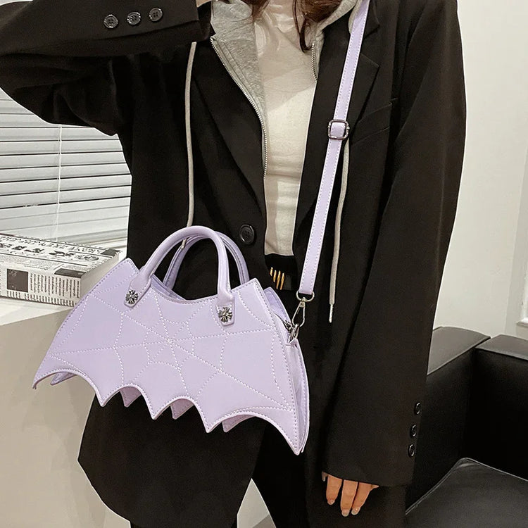 Woman wearing oversized black blazer, gray hoodie, and white shirt, holding a pastel purple bat-shaped handbag with top handle and shoulder strap.