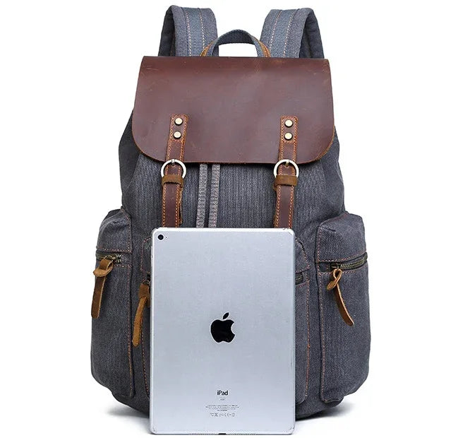 Gray canvas backpack with brown leather flap, front pockets, and relaxed fit, displayed with tablet
