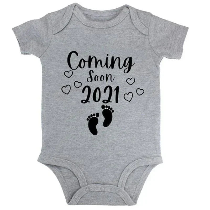 Gray cotton baby bodysuit with short sleeves, black 'Coming Soon 2021' print, heart and footprint design, soft and comfortable fit.