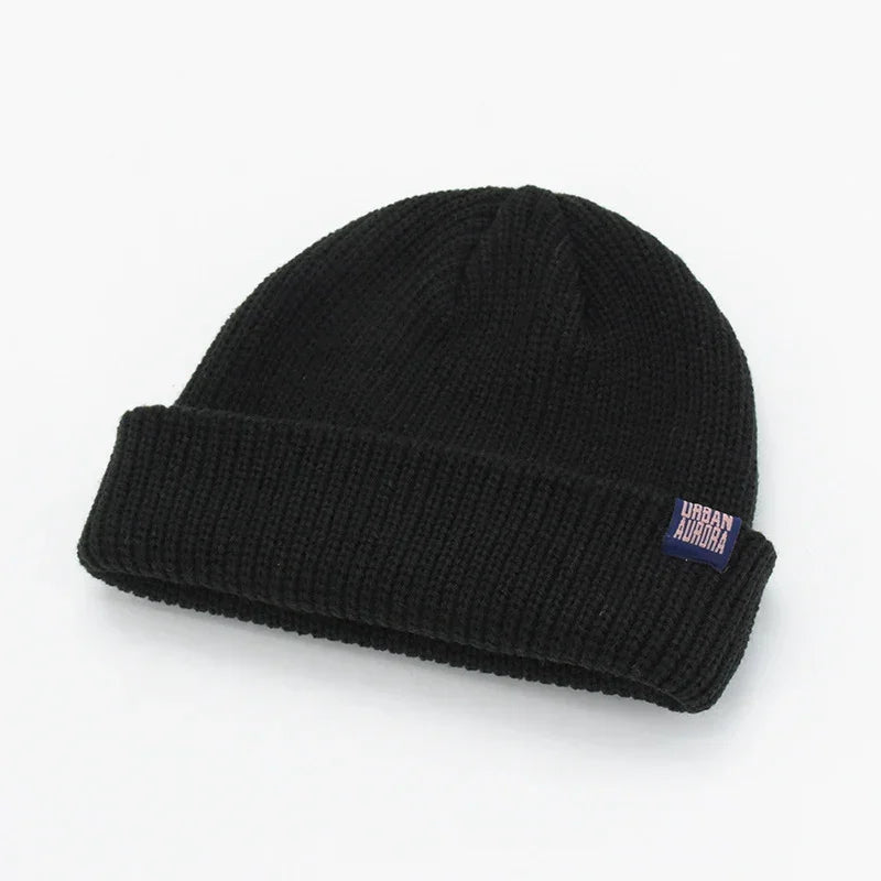 Black ribbed knit beanie with fold-over cuff, relaxed fit, small woven label on edge.