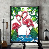 Framed wall art of two pink flamingos standing in blue water with green tropical leaves