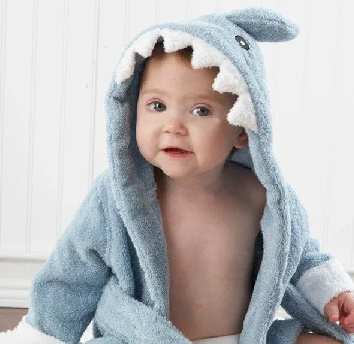 Baby wearing blue plush hooded robe with shark design, featuring soft texture and loose fit.