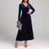 Woman wearing a navy blue velvet long-sleeve maxi dress with a V-neck and fitted waist.