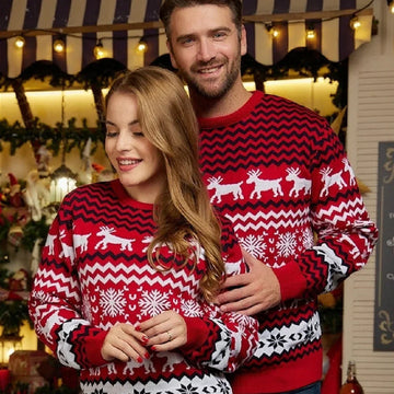 Couple wearing matching red and white knit Christmas sweaters with reindeer and snowflake patterns