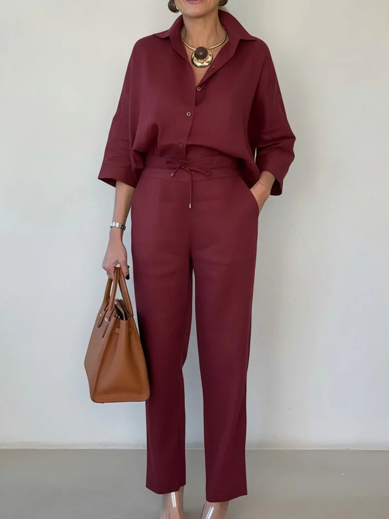 Woman wearing loose-fit burgundy button-up shirt and matching trousers with brown handbag